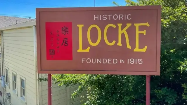 Uma placa marrom com os escritos 'Distrito histórico de Locke, fundado em 1915', em inglês, e, ao lado esquerdo, os escritos em ideograma chinês.