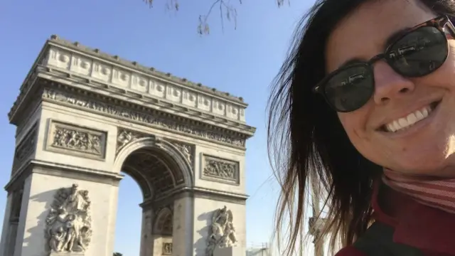 M. E. Thomas de óculos escuros sorrindo em frente a um monumento