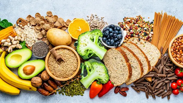 Alimentos ricos em fibras dispostos lado a lado, como banana, tomates, brócolis, oleoginosas, mirtilo e tâmaras